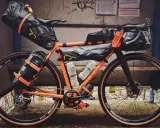 Orange Rennrad mit Bikepacking-Taschen, bereit für Abenteuer.