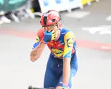 Radfahrer Thibau Nys wischt sich mit der Hand über das Gesicht, trägt einen roten Helm und ein blau-gelbes Trikot.