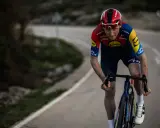 Tao Geoghegan Hart im roten Trikot auf einer kurvigen Straße, konzentriert auf das Rennen.