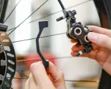 Hände montieren eine Fahrrad-Scheibenbremse. Ein Adapter wird gehalten, um ein Schleifen der Scheibenbremse zu verhindern.
