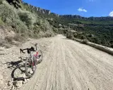 Ein Rennrad steht auf einer staubigen Straße in Sardinien, umgeben von felsigen Hängen und grüner Vegetation.