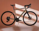 Ein Gravelbike in einem sanften Sandton, das wie ein Kunstwerk schwebt. Der Rahmen und die Reifen bilden einen harmonischen rose blend mit dem Hintergrund.