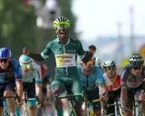 Biniam Girmay jubelt im grünen Trikot nach einem Sieg. Radprofis im Rennen.