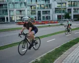 Zwei Rennradfahrerinnen genießen eine Fahrt auf einem Radweg vor modernen Gebäuden.