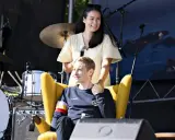 Jonas Vingegaard sitzt im Sessel, seine Frau hält ihn liebevoll. Im Hintergrund ist eine Bühne mit Schlagzeug.