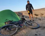 Mann mit Fahrrad und Zelt in bergiger Landschaft, bereit für neue **biking trails**.