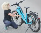Frau mit lockigem Haar lädt den Akku eines hellblauen E-Bikes.