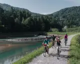 Gruppe genießt MTB Touren entlang eines Flusses mit bewaldeten Hügeln im Hintergrund.
