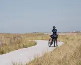 Frau mit Fahrrad auf einer Küstenstraße, bereit für eine Fahrradtour in der Nähe von Amsterdam.