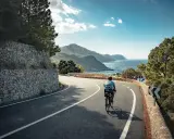 Rennradfahrer auf einer kurvigen Straße mit Blick auf das Meer und die Berge auf Mallorca.