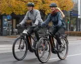 Ein Mann und eine Frau fahren mit ihren Pedelecs durch die Stadt. Was ist ein Pedelec? Ein Fahrrad mit elektrischer Unterstützung, das das Fahren erleichtert.