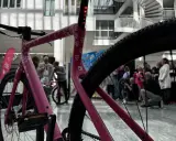 Ein pinkes company bike der Telekom mit vielen T-Logos. Im Hintergrund stehen Menschen und eine Wendeltreppe.
