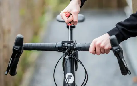Hände stellen den MTB Lenker ein. Mit einem Schraubenzieher wird die Lenkerposition justiert, um die perfekte Fahrt zu ermöglichen.