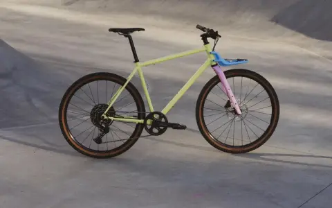 Ein gelbes Fahrrad mit rosa Gabel und blauem Gepäckträger, bereit für eine Fahrt durch die Stadt. Rose black lava 2 test.