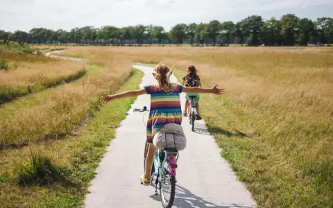 Zwei Mädchen genießen eine Fahrradtour in NRW auf einem Feldweg, umgeben von goldenem Gras und Bäumen.