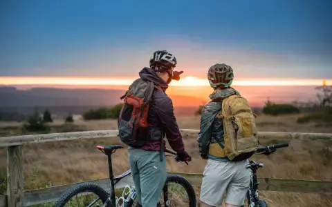 Zwei Radfahrer blicken bei Sonnenuntergang auf die Landschaft. Ein Mann zeigt in die Ferne, vielleicht auf den Stoneman Arduenna.