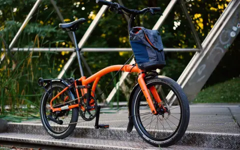Orange Brompton Electric im Test auf einer Metallbrücke, bereit für die nächste Fahrt.