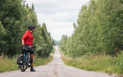 Frauen auf Bikepacking-Tour in Schweden, bereit für die nächste Etappe auf einer einsamen Schotterstraße, umgeben von üppigem Grün.