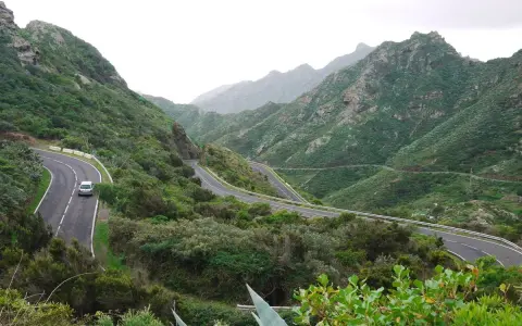 Serpentinenstraße auf Teneriffa, ideal für eine Rennradtour durch grüne Berge. Ein Auto fährt auf der kurvenreichen Straße.