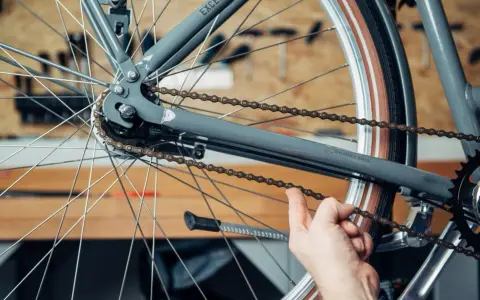 Hand prüft die Spannung der Fahrradkette am Hinterrad eines grauen Fahrrads.
