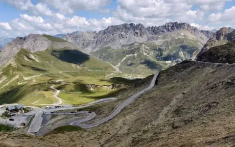 Bergpanorama mit Serpentinenstraße, grasbewachsenen Hängen und schroffen Gipfeln.