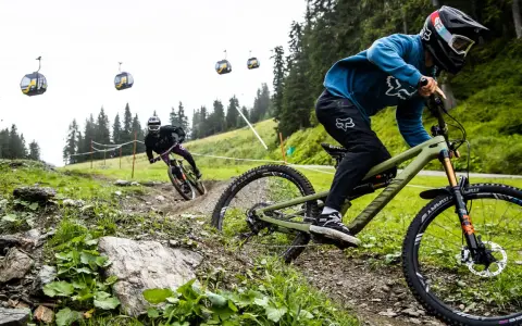 Zwei Mountainbiker auf einem steilen Trail, Seilbahnen im Hintergrund. Einer fährt ein Rad mit Mullet-Setup, was ist ein Mullet?