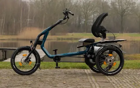 Ein tealfarbenes Easy Rider Bike mit drei Rädern steht am Wasser. Es hat einen bequemen Sitz und eine hohe Rückenlehne.