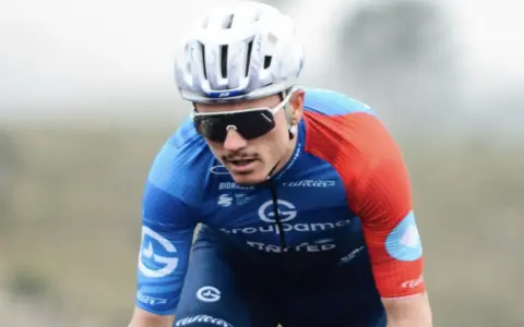 David Gaudu im blauen und roten Trikot, mit Helm und Sonnenbrille, konzentriert sich auf das Rennen.