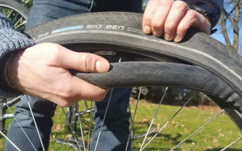 Hände wechseln einen platten Fahrradreifen. Der Reifen ist ein Schwalbe Big Ben.