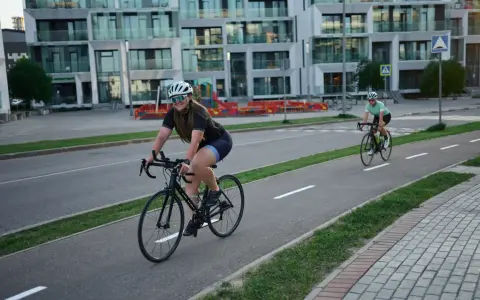 Zwei Rennradfahrerinnen genießen eine Fahrt auf einem Radweg vor modernen Gebäuden.