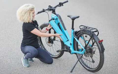 Frau mit lockigem Haar lädt den Akku eines hellblauen E-Bikes.