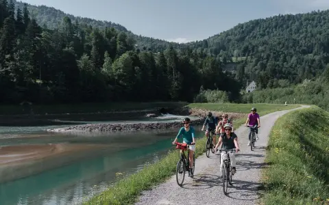 Gruppe genießt MTB Touren entlang eines Flusses mit bewaldeten Hügeln im Hintergrund.