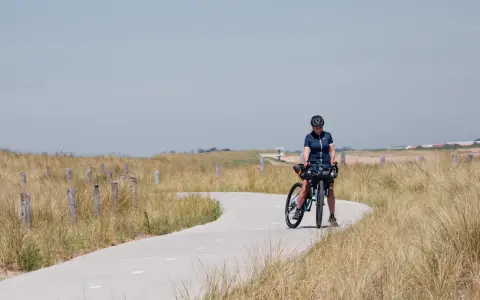 Frau mit Fahrrad auf einer Küstenstraße, bereit für eine Fahrradtour in der Nähe von Amsterdam.