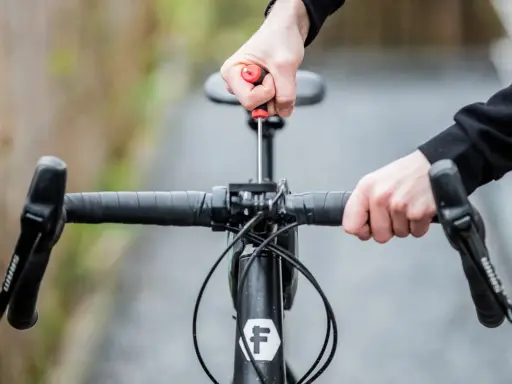 Hände stellen den MTB Lenker ein. Mit einem Schraubenzieher wird die Lenkerposition justiert, um die perfekte Fahrt zu ermöglichen.