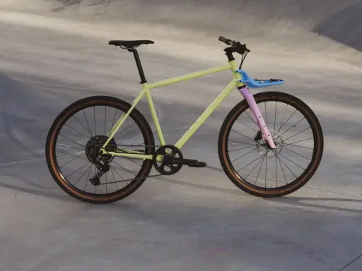 Ein gelbes Fahrrad mit rosa Gabel und blauem Gepäckträger, bereit für eine Fahrt durch die Stadt. Rose black lava 2 test.