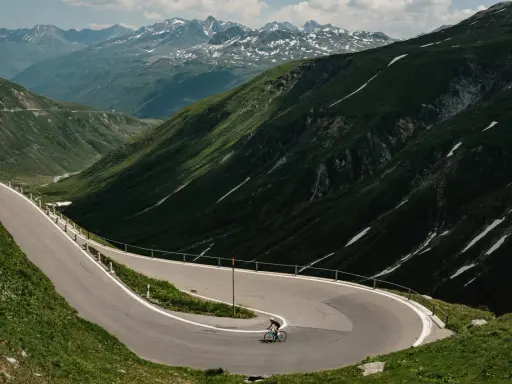 Radfahrer auf einem Transalp Rennrad meistert Serpentinen in den Alpen. Majestätische Bergkulisse mit Schneefeldern.