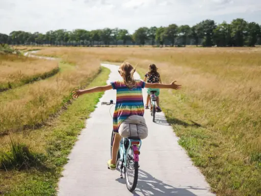 Zwei Mädchen genießen eine Fahrradtour in NRW auf einem Feldweg, umgeben von goldenem Gras und Bäumen.