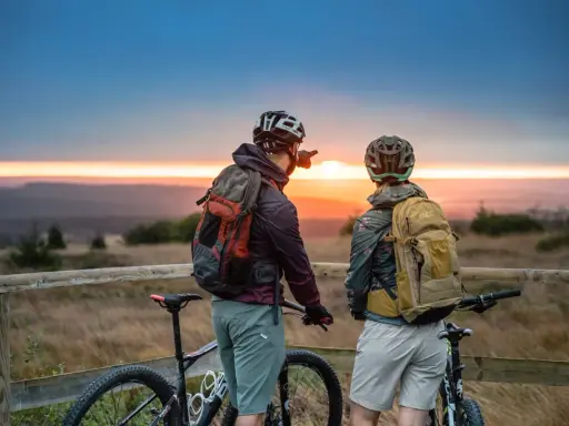 Zwei Radfahrer blicken bei Sonnenuntergang auf die Landschaft. Ein Mann zeigt in die Ferne, vielleicht auf den Stoneman Arduenna.