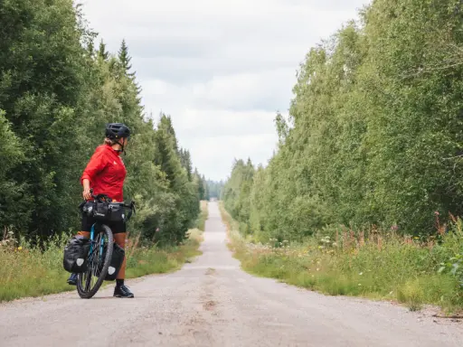 Frauen auf Bikepacking-Tour in Schweden, bereit für die nächste Etappe auf einer einsamen Schotterstraße, umgeben von üppigem Grün.