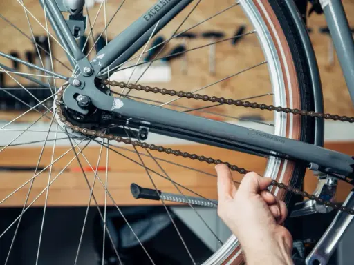 Hand prüft die Spannung der Fahrradkette am Hinterrad eines grauen Fahrrads.