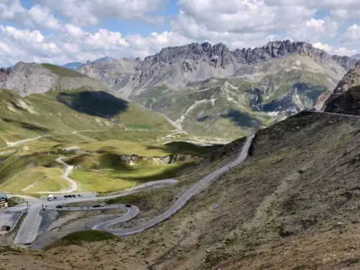Bergpanorama mit Serpentinenstraße, grasbewachsenen Hängen und schroffen Gipfeln.