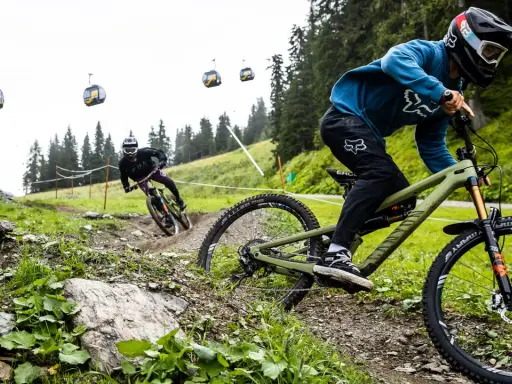 Zwei Mountainbiker auf einem steilen Trail, Seilbahnen im Hintergrund. Einer fährt ein Rad mit Mullet-Setup, was ist ein Mullet?