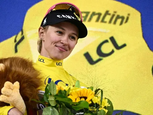 Kasia Niewiadoma strahlt im gelben Trikot, hält einen Löwen-Plüschtier und Blumen.