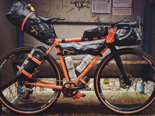 Orange Rennrad mit Bikepacking-Taschen, bereit für Abenteuer.