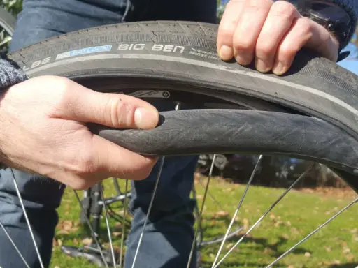 Hände wechseln einen platten Fahrradreifen. Der Reifen ist ein Schwalbe Big Ben.