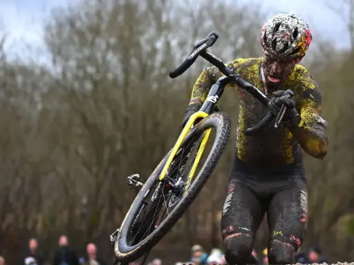 Wout van Aert kämpft sich im Schlamm durch ein hartes Cyclocross-Rennen, sein Körper und Rad sind komplett mit Dreck bedeckt.