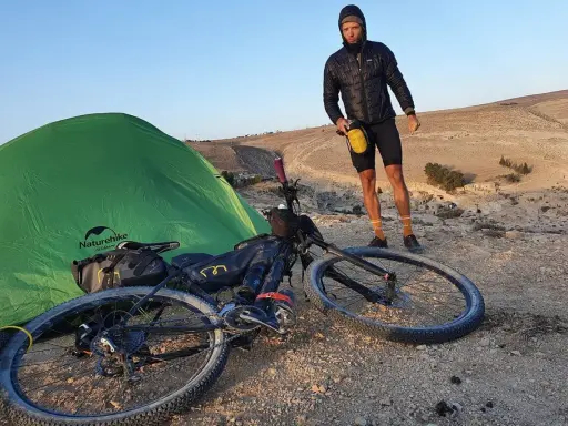 Mann mit Fahrrad und Zelt in bergiger Landschaft, bereit für neue **biking trails**.