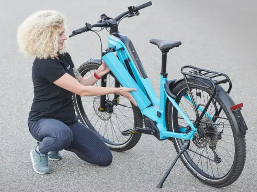 Frau mit lockigem Haar lädt den Akku eines hellblauen E-Bikes.