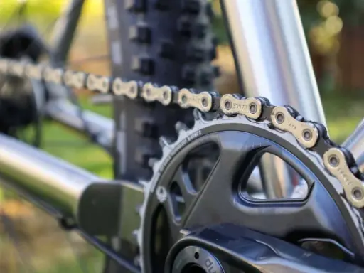 Nahaufnahme einer Fahrradkette, die über ein Kettenblatt läuft. Die Kette zeigt deutliche Gebrauchsspuren, was auf die Shimano Ketten Unterschiede in Bezug auf Haltbarkeit und Leistung hinweist.