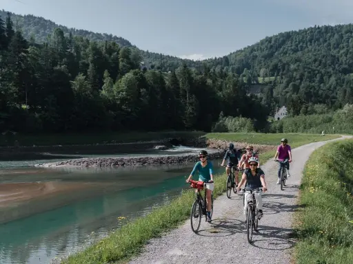 Gruppe genießt MTB Touren entlang eines Flusses mit bewaldeten Hügeln im Hintergrund.